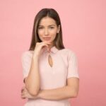 Portrait of a young woman posing elegantly in a studio with a pink background.